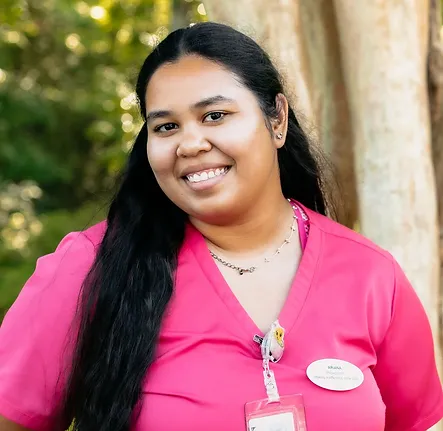 Ariana, a member of the checkout staff at Bloom Aesthetics and Wellness, poses outside smiling wearing pink scrubs.
