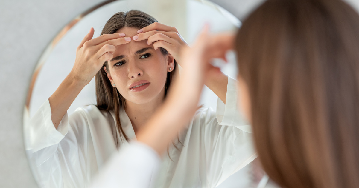 woman touching her forehead and looking in a mirror